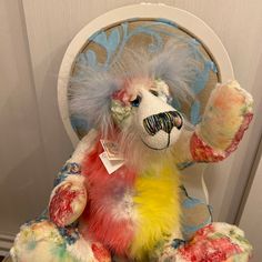 a colorful stuffed animal sitting on top of a chair with its arms in the air