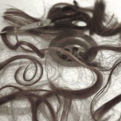 scissors and hair are laying on top of the pile of long brown hair that has been cut in half