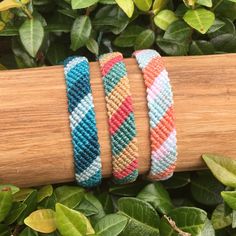 three different bracelets sitting on top of a wooden stick in front of green leaves