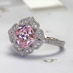 The Platinum Plated Sterling Silver Ring, Cushion Super Light Pink CZ Stone Milgrain Vintage 2 carat Engagement Ring, Pink Diamond Simulant Ring Cocktail Ring (Size 5 to 9) is nothing short of breathtaking. With its vintage-style vibe, it showcases an eye-catching light pink cushion cut cubic zirconia encircled by sparkling round cut accents set in milgrain edge finish petals being formed a heart shape. It would be a sensation at a garden party and a lovely complement to your little black dress Pink Diamond Promise Ring With Halo Design, Elegant Pink Flower Ring For Anniversary, Classic Pink Cluster Ring For Anniversary, Elegant Pink Cluster Promise Ring, Pink Diamond Ring With Gemstone For Promise, Pink Topaz Center Stone Ring For Anniversary, Pink Diamond Ring With Halo Design For Anniversary, Pink Cluster Ring With Center Stone For Anniversary, Pink Halo Diamond Ring For Anniversary