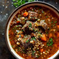 a bowl filled with beef and barley soup on top of a table next to some parsley