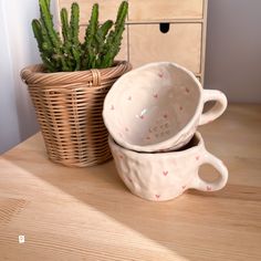 two white cups sitting on top of a wooden table next to a potted plant