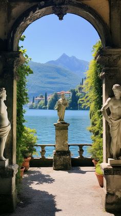 an archway with statues on either side leading to a lake and mountains in the distance