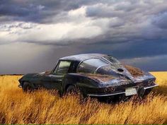 an old car sitting in the middle of a field under a cloudy sky with storm clouds