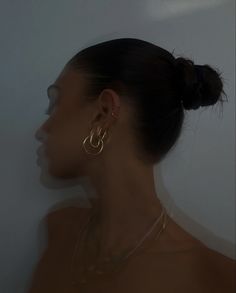 a woman wearing large gold hoop earrings in front of a white wall