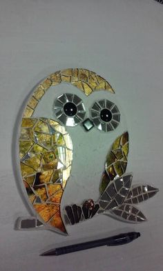 an owl made out of broken glass sitting on top of a white table next to a pen