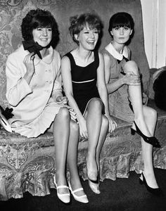 three women are sitting on a bed and posing for the camera, with one woman holding her leg up