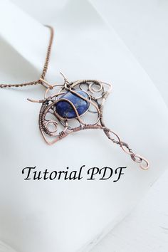 a wire wrapped necklace with a blue stone in the center on a white cloth background