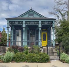 a blue house with a yellow door in the middle of some bushes and shrubbery