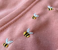 three bees on pink sweaters with yellow and black pins in the middle, sitting on top of each other