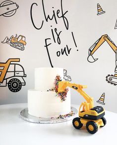 a white cake with yellow construction vehicles on it and a sign that says chick fil's four