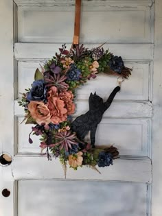 a wreath with flowers and a cat hanging on the front door to decorate it for someone's house