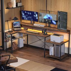 a computer desk with two monitors and a laptop on it in front of a wooden wall