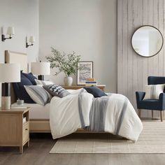 a bedroom with white and blue bedding, two chairs and a mirror on the wall