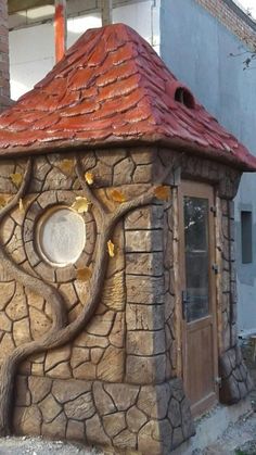 a small building made out of rocks with a tree on the outside and a round window