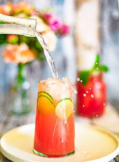 a drink being poured into a glass on top of a plate with flowers in the background