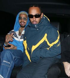 two men sitting in the back of a car, one holding a cell phone and smiling