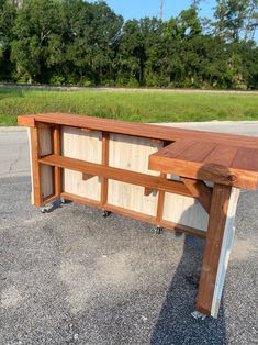 a wooden bench sitting in the middle of a parking lot next to a grassy field