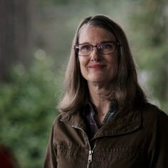 a woman wearing glasses standing in front of trees