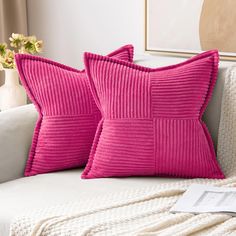 two pink pillows sitting on top of a white couch next to a vase with flowers