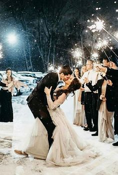 a bride and groom kissing in the snow surrounded by sparklers