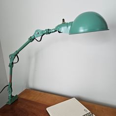 a green desk lamp sitting on top of a wooden table next to a laptop computer