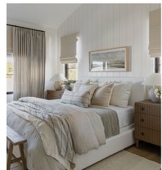 a white bed sitting next to a window covered in curtains and pillows on top of a wooden dresser