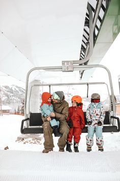 three people sitting on a ski lift with one holding a baby and the other standing up