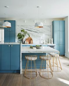 a kitchen with blue cabinets and marble counter tops, gold barstools and stools