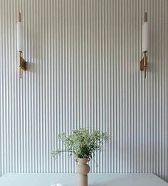 a vase with flowers on a table in front of a wall mounted light fixture and two sconces