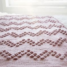 a crocheted blanket is laying on a white rug in front of a window