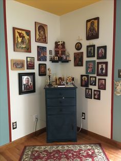 a blue dresser sitting in the corner of a room with many pictures on the wall