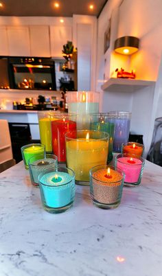 there are many different colored candles on the counter top in front of the kitchen sink