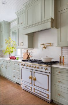 a large kitchen with green cabinets and white counter tops, gold pulls on the handles