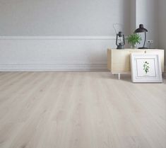 an empty room with white walls and wood flooring is pictured in this image, there are two framed photographs on the sideboard