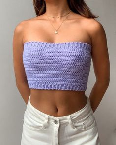 a woman in white shorts and a purple crop top is posing for the camera with her hands on her hips