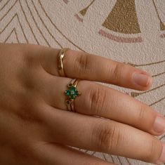 a woman's hand wearing a gold ring with green stones on the middle finger