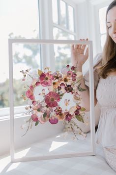 a woman holding up a flower arrangement in front of a window