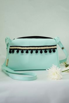 a mint green purse with pom - poms on the side and a flower next to it