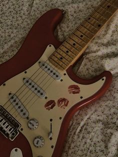 a red electric guitar laying on top of a bed covered in blankets and sheets with lipstick prints