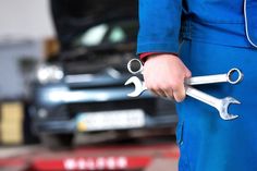 a man in blue uniform holding two wrenches