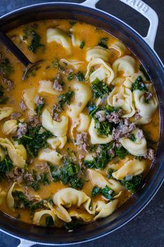 a pot filled with pasta, meat and spinach in broth next to a spoon