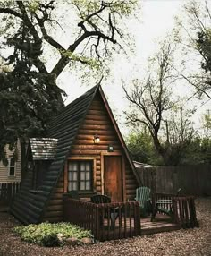 a small log cabin sits in the middle of a yard with two lawn chairs on it