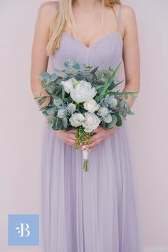 a woman in a purple dress holding a bouquet of white flowers and greenery on her wedding day