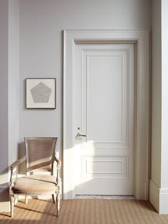 an empty chair in front of a door with a painting on the wall next to it