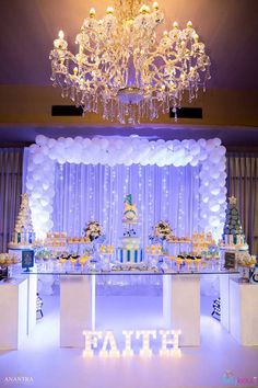 a decorated dessert table with white balloons and blue lights on the ceiling is lit by a chandelier that reads faith