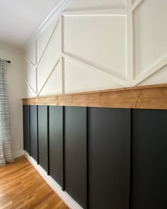 an empty room with black paneling and wood flooring on the wall, in front of a window