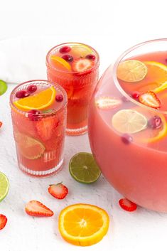 two glasses filled with liquid and fruit next to sliced lemons, strawberries, and lime slices