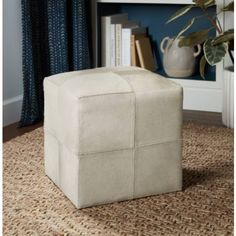 a square footstool on a rug in front of a book shelf with books