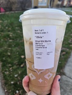 a person holding up a plastic cup with information on the side of it in front of a house